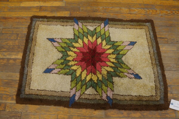 Textured rug with a multi-colored star design and thick brown border on plank wood floors.