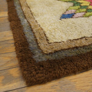 High-pile rug corner showing brown borders, cream field, and multicolor floral motifs on distressed wood.