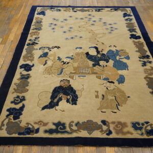 Low-pile beige rug with blue figures and a dark border, placed on worn yellow hardwood planks.
