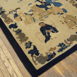 Low-pile tan rug with a blue figural pattern, framed by a dark navy border, resting on wood planks.