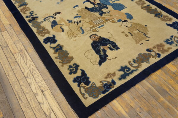 Low-pile tan rug with a blue figural pattern, framed by a dark navy border, resting on wood planks.