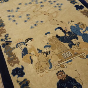 Low-pile beige rug with a blue and brown figural scene and wide navy border rests on wood flooring.