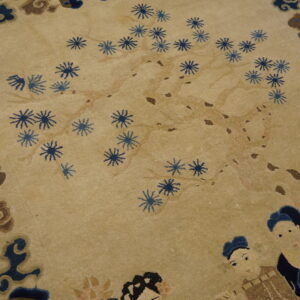 Beige field rug with blue floral sprays, stylized figures, and a dark blue and brown pictorial border.