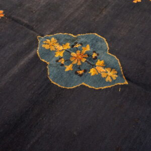 Dark blue rug detail featuring a stylized teal leaf shape with intricate gold and orange floral motifs.