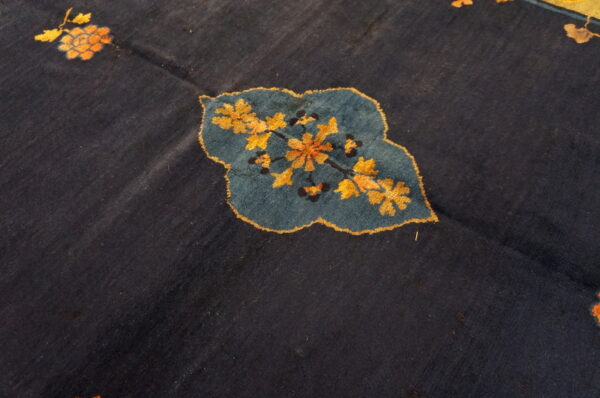 Dark blue rug detail featuring a stylized teal leaf shape with intricate gold and orange floral motifs.