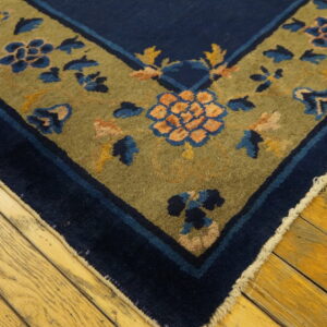 Low-pile rug corner showing navy blue and olive green borders with floral motifs on hardwood flooring.