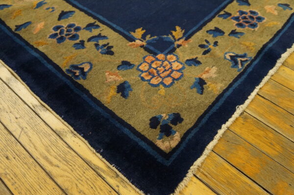 Low-pile rug corner showing navy blue and olive green borders with floral motifs on hardwood flooring.