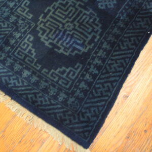 Dark navy rug corner with interlocking geometric patterns in faded blue rests on light wood flooring.