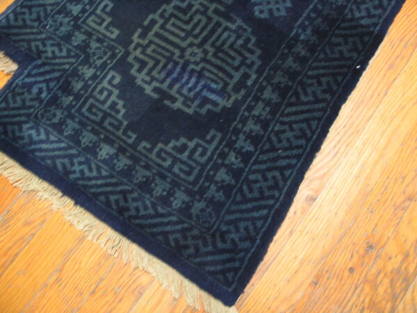 Dark navy rug corner with interlocking geometric patterns in faded blue rests on light wood flooring.
