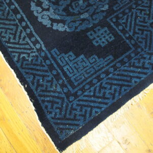 Dark blue rug featuring geometric and scrolling patterns rests on light wood floorboards.
