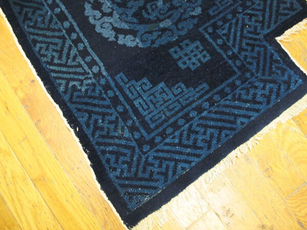 Dark blue rug featuring geometric and scrolling patterns rests on light wood floorboards.