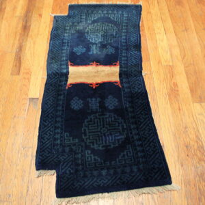 Dark blue runner rug with geometric teal patterns and a tan stripe shown on light wooden planks.