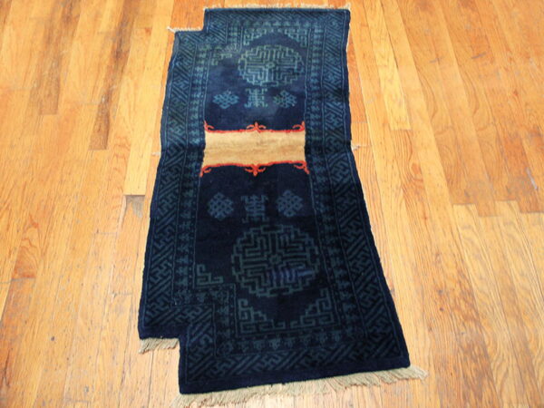 Dark blue runner rug with geometric teal patterns and a tan stripe shown on light wooden planks.