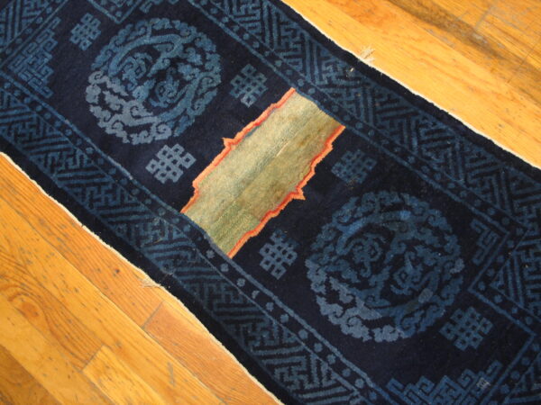 Navy blue runner rug with light blue patterns and a central green and coral patch rests on wood floors.