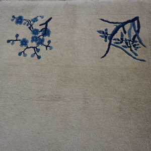 Muted beige rug with navy and light blue floral patterns resting on rustic wood flooring.