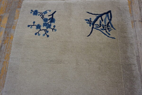 Muted beige rug with navy and light blue floral patterns resting on rustic wood flooring.