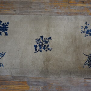 Muted beige rug with dark indigo floral designs and fringe, set on rustic wood planks.