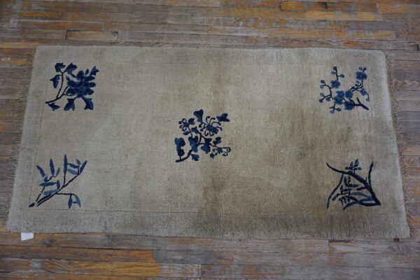 Muted beige rug with dark indigo floral designs and fringe, set on rustic wood planks.