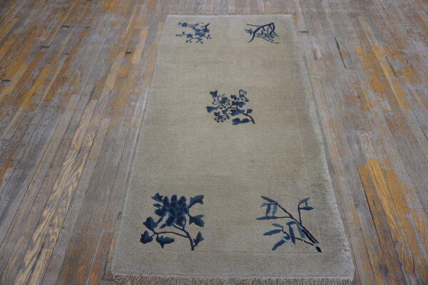 Neutral runner rug with indigo floral motifs displayed on aged, light brown wood planks.