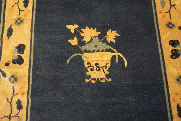 Dark blue rug detail showing a golden vase and floral motif next to a tan patterned border.