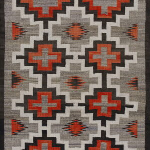Geometric flatweave rug with repeating step and cross motifs in gray, white, dark brown, and bright orange.