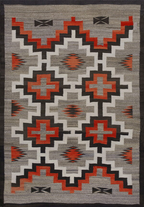 Geometric flatweave rug with repeating step and cross motifs in gray, white, dark brown, and bright orange.