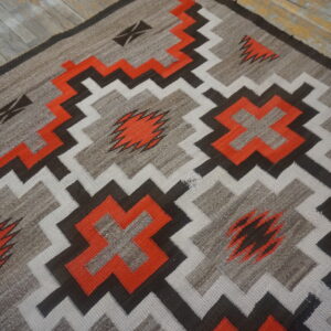 Flatweave rug with bright orange, gray, white, and brown geometric patterns on rustic wood floor.