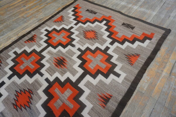 Geometric rug featuring stepped crosses and zigzags in orange, gray, black, and cream on distressed wood planks.