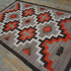 Geometric flatweave rug featuring stepped diamonds and zigzag patterns in orange, white, and dark brown on distressed wood floors.