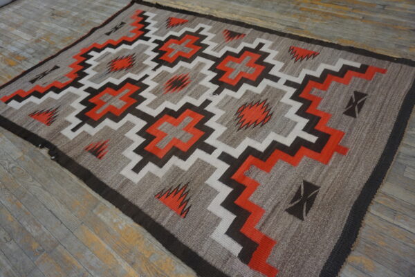 Geometric flatweave rug featuring stepped diamonds and zigzag patterns in orange, white, and dark brown on distressed wood floors.
