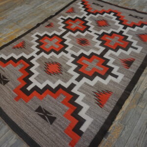 Southwestern geometric rug in tan, bright orange, dark brown, and white on rustic wood flooring.
