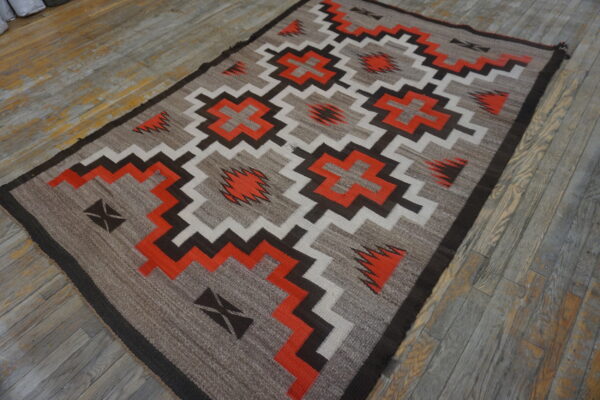 Southwestern geometric rug in tan, bright orange, dark brown, and white on rustic wood flooring.