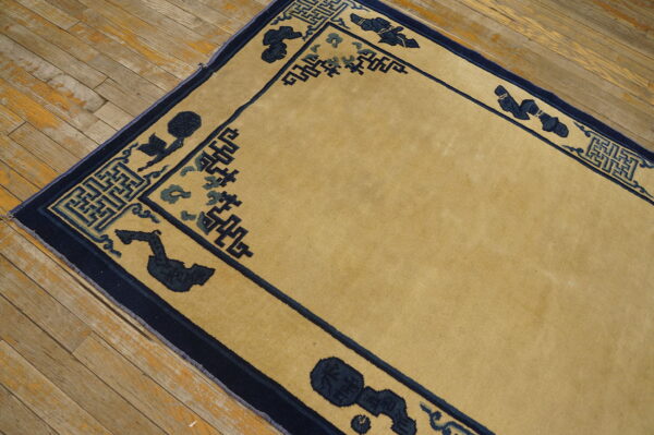 Gold rug with navy border featuring key patterns and abstract motifs on worn hardwood flooring.