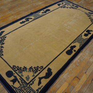 A rectangular tan rug with a navy and blue stylized border sits on worn wooden plank flooring.