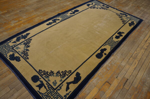 A rectangular tan rug with a navy and blue stylized border sits on worn wooden plank flooring.