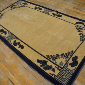 Low-pile beige rug with complex navy blue and teal borders on weathered wooden plank floors.