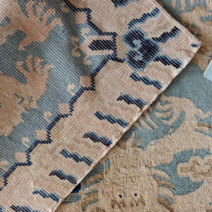Detail shot of a rug folded, contrasting the plush beige and teal pile with a flat navy-trimmed back.