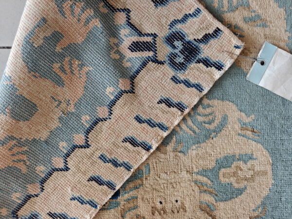 Detail shot of a rug folded, contrasting the plush beige and teal pile with a flat navy-trimmed back.