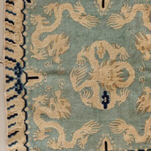 Close-up of a teal rug featuring beige dragon motifs and a border detailed with dark blue accents.
