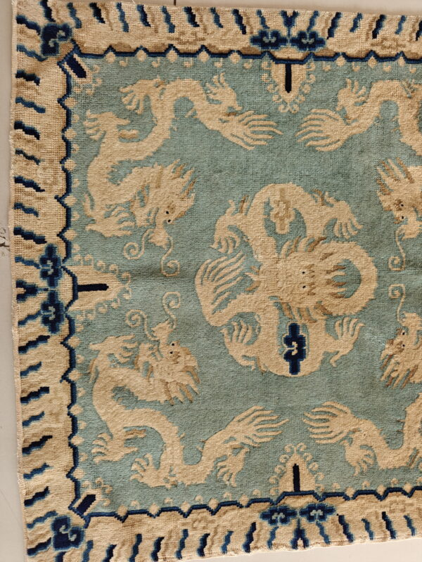 Close-up of a teal rug featuring beige dragon motifs and a border detailed with dark blue accents.