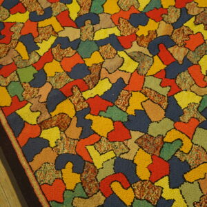 Multicolored loop pile rug features an abstract pattern of irregular shapes set against light wood flooring.