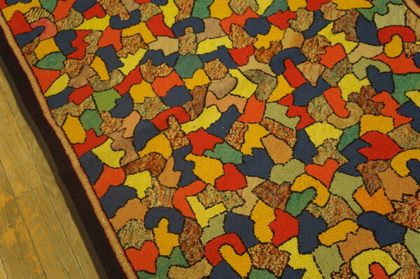 Multicolored loop pile rug features an abstract pattern of irregular shapes set against light wood flooring.