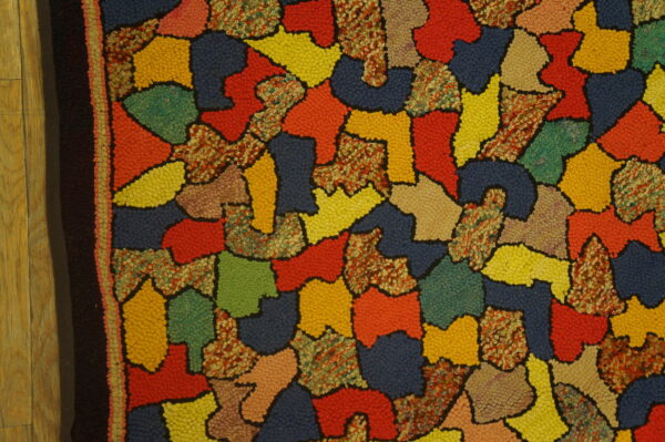 Nubby textured rug with a colorful abstract pattern and dark border lying on light wood flooring.