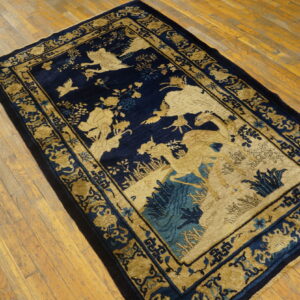 A low-pile navy blue rug features detailed golden bird and deer motifs on a distressed wood plank floor.
