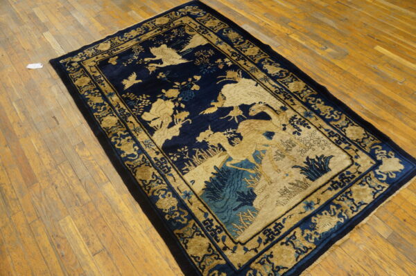 A low-pile navy blue rug features detailed golden bird and deer motifs on a distressed wood plank floor.