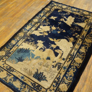 Navy and tan rug with a scenic pattern of animals and foliage, bordered by geometric motifs, on wood plank flooring.