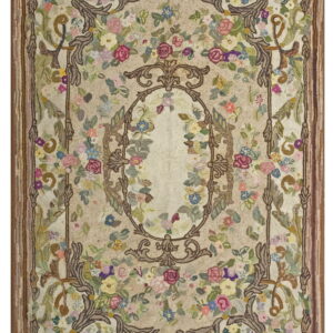 Textured hooked rug featuring a beige field, ornate brown scrollwork, and dense multicolored floral motifs throughout.