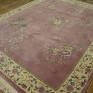 Mauve pile rug with floral bouquets and birds on a patterned cream border, displayed on plank wood flooring.