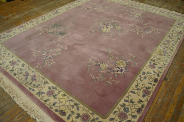 Mauve pile rug with floral bouquets and birds on a patterned cream border, displayed on plank wood flooring.