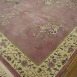Mauve floral rug with carved details, a cream border featuring vines and birds, laying on hardwood floors.